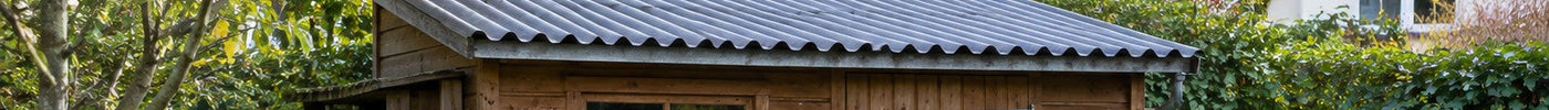 Holz-Gartenhaus mit Pultdach aus anthrazitfarbenen Wellplatten in einem Garten am Einfamilienhaus – Deutsche Kunststoffbedachungen