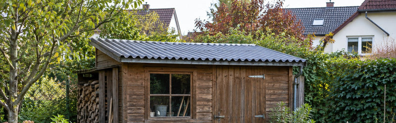 Holz-Gartenhaus mit Pultdach aus anthrazitfarbenen Wellplatten in einem Garten am Einfamilienhaus – Deutsche Kunststoffbedachungen