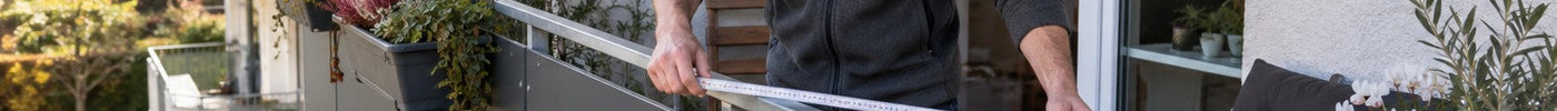 Mann misst ein Balkongeländer mit Maßband aus, um die Balkonverkleidung mit anthrazitfarbenen HPL-Platten zu berechnen – Deutsche Kunststoffbedachungen