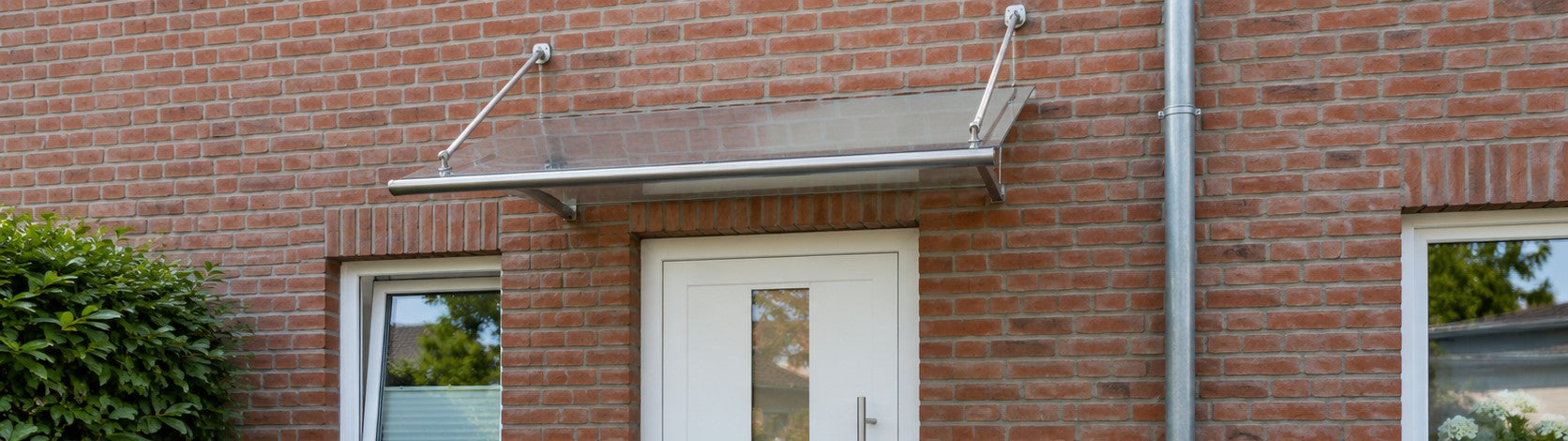 Pultvordach mit klarem Acrylglas und Edelstahl-Tragarmen über der Haustür eines Klinker-Reihenhauses – Deutsche Kunststoffbedachungen