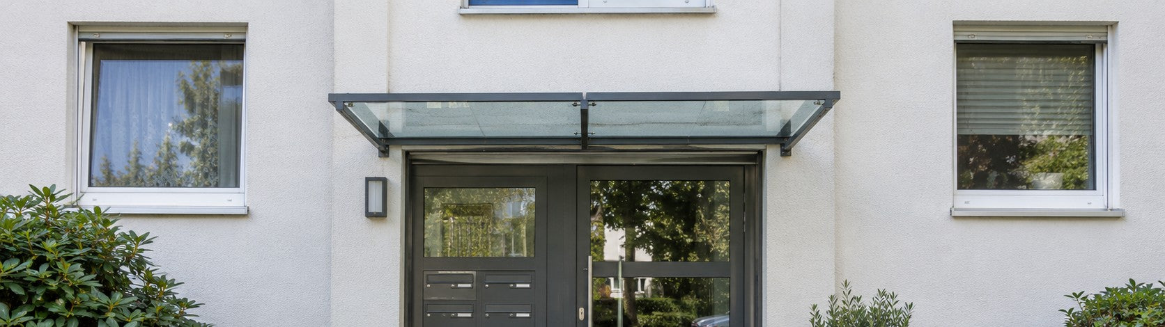 Vordach aus Glas über dem gemeinsamen Hauseingang eines Mehrfamilienhauses – Deutsche Kunststoffbedachungen