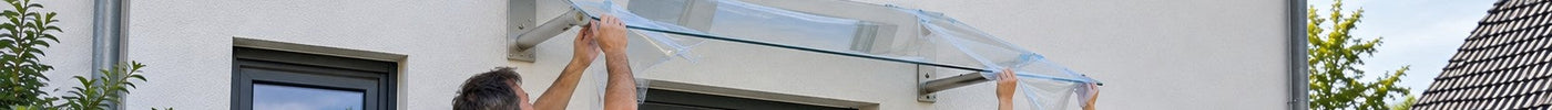 Zwei Heimwerker setzen eine neue Acrylglas-Scheibe auf das Vordach über der Haustür eines Einfamilienhauses – Deutsche Kunststoffbedachungen